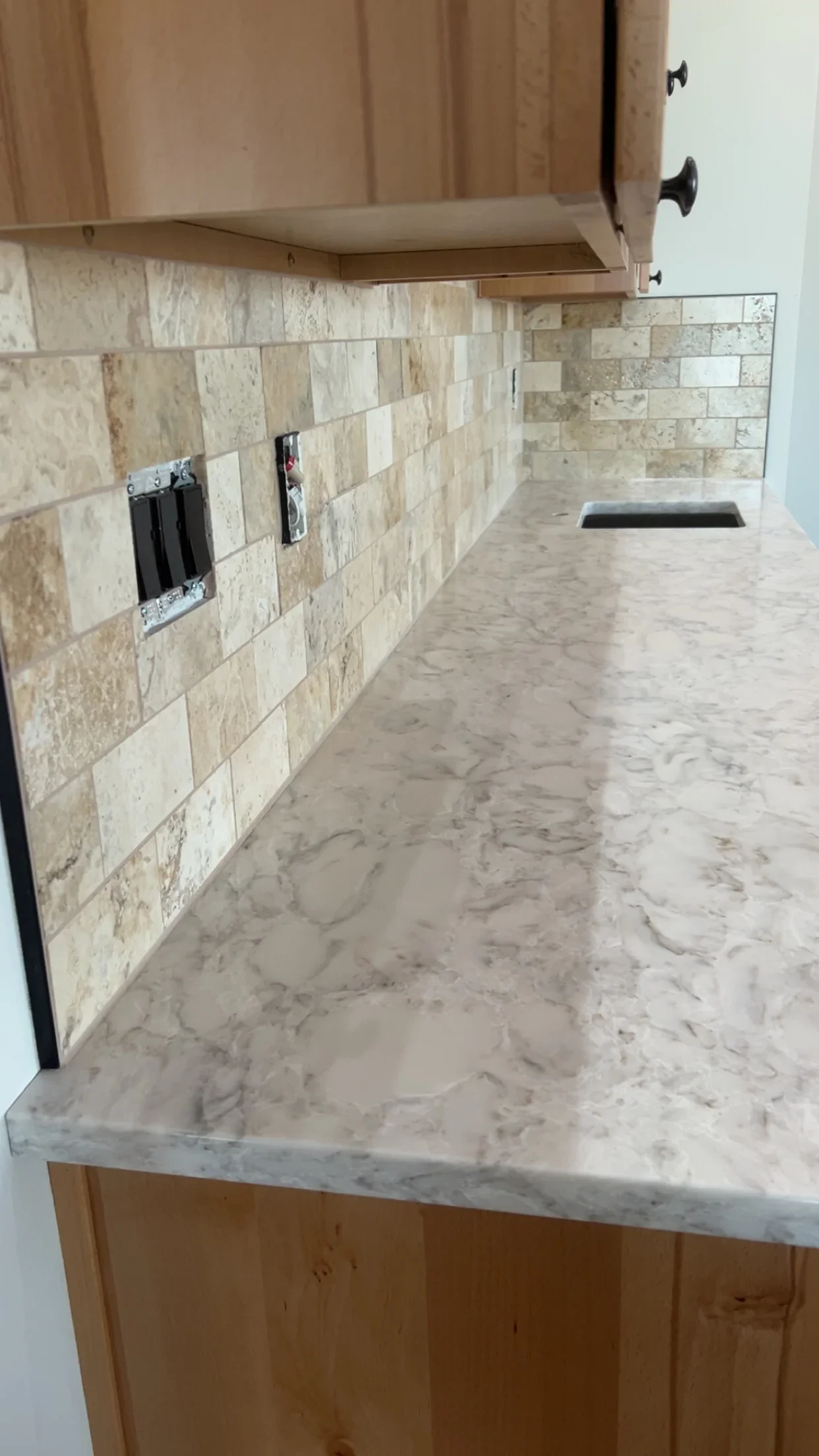 Travertine tile backsplash and marble countertop kitchen installation with electrical outlets