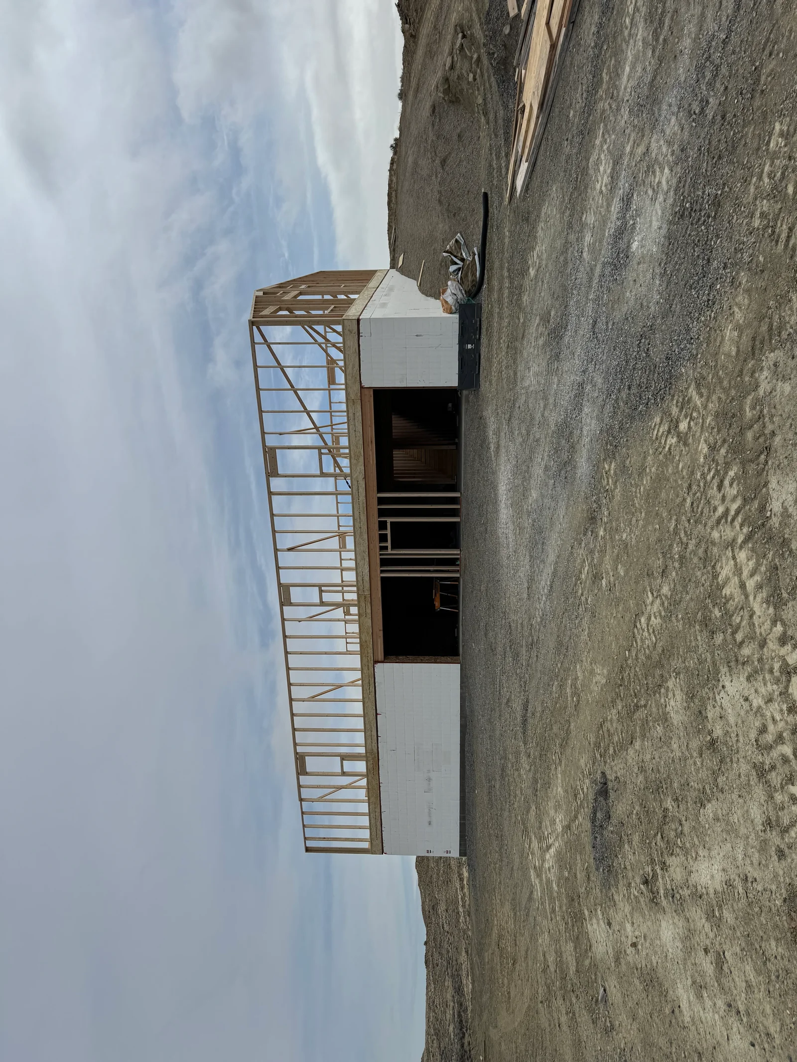 Concrete foundation and stem wall with steel frame and wood roof trusses under construction