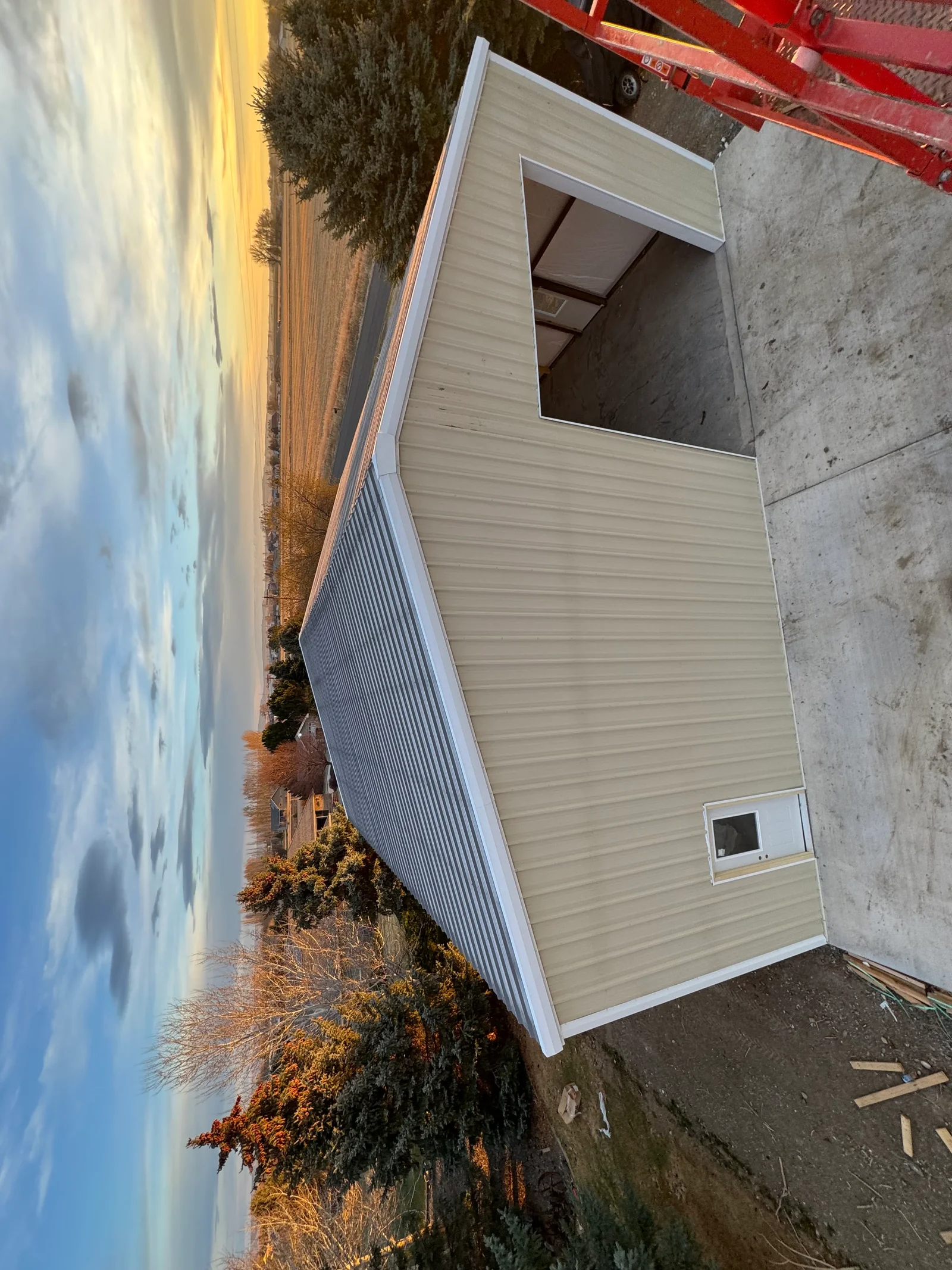Light gray corrugated metal building with white trim and window openings on concrete foundation