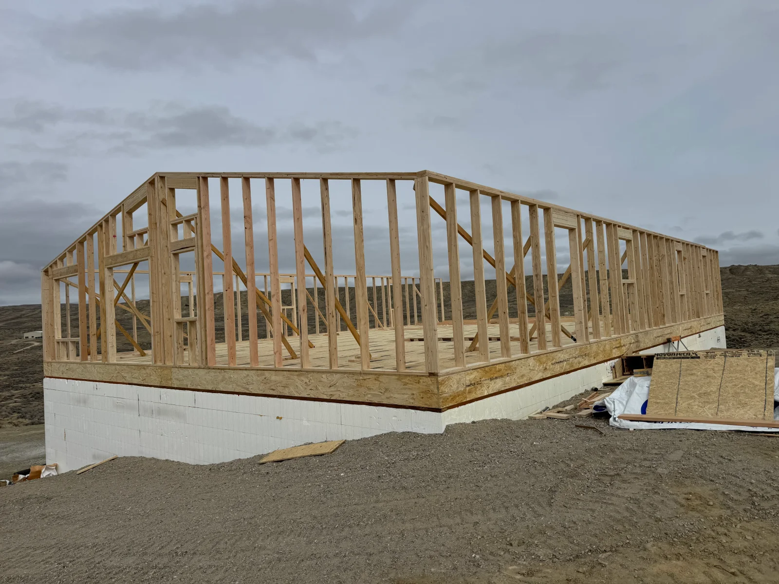 Wooden frame structure with dimensional lumber framing, cross-bracing, and window openings on concrete foundation