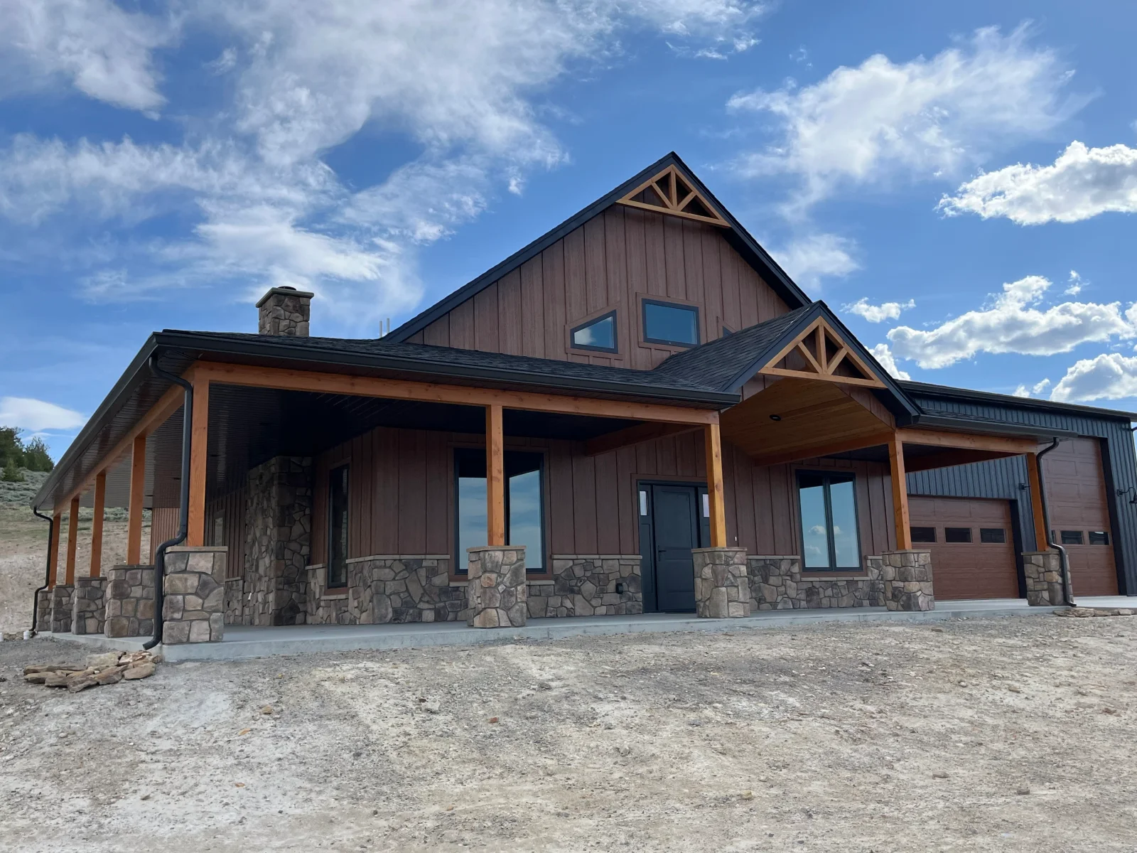 Modern home with stacked stone base, brown metal siding, timber gable frames, and metal roof