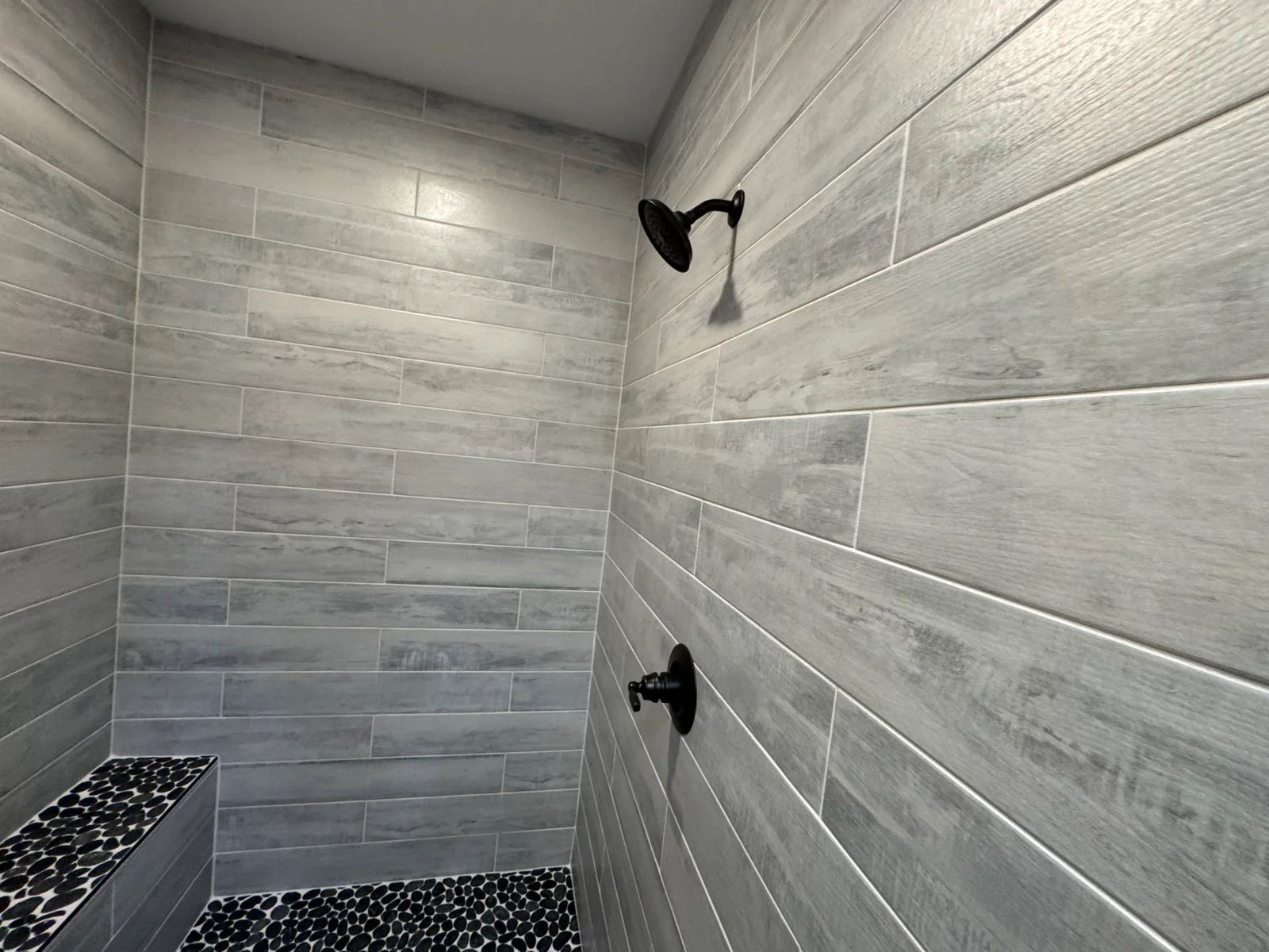 Gray wood-look porcelain tile shower with black fixtures and pebble stone floor