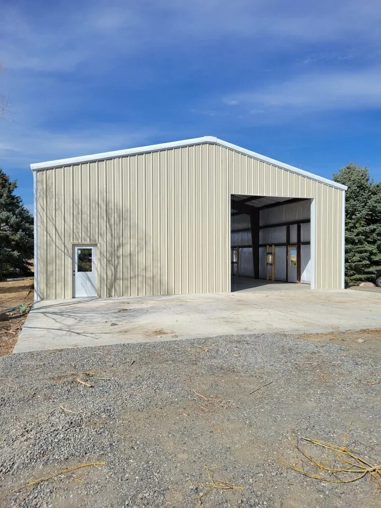 White metal building with vertical corrugated siding, black garage doors, and concrete apron
