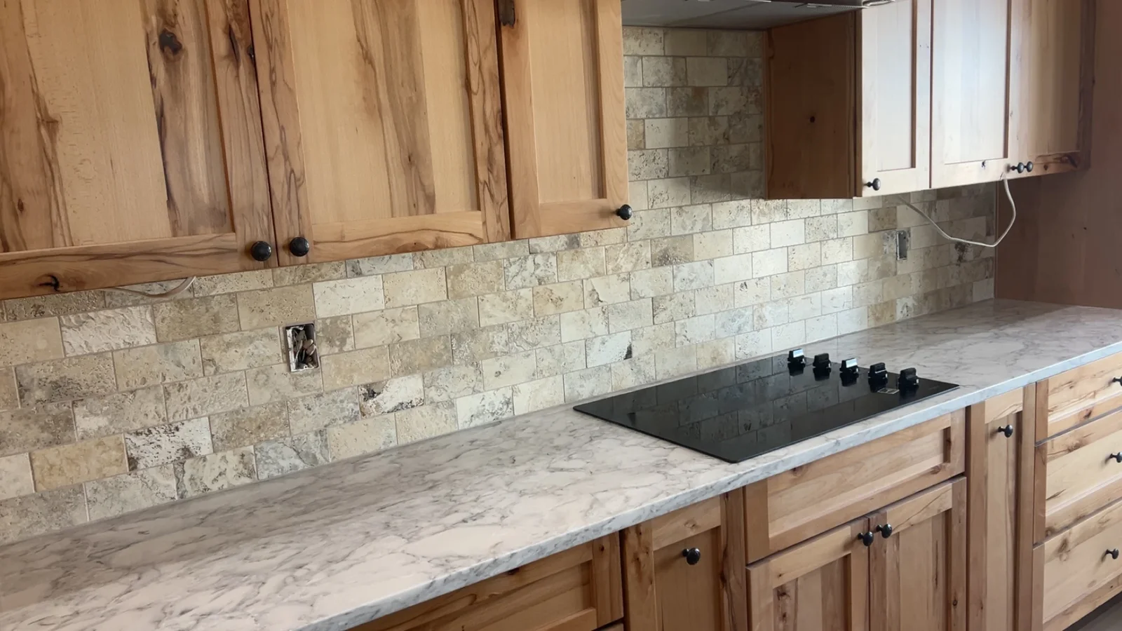 Kitchen with wood cabinets, marble countertop, and travertine subway tile backsplash