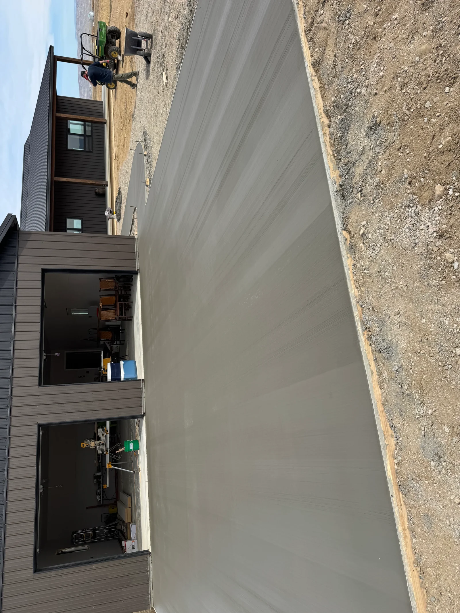 Freshly poured concrete driveway with smooth gray finish next to dark-sided residential building