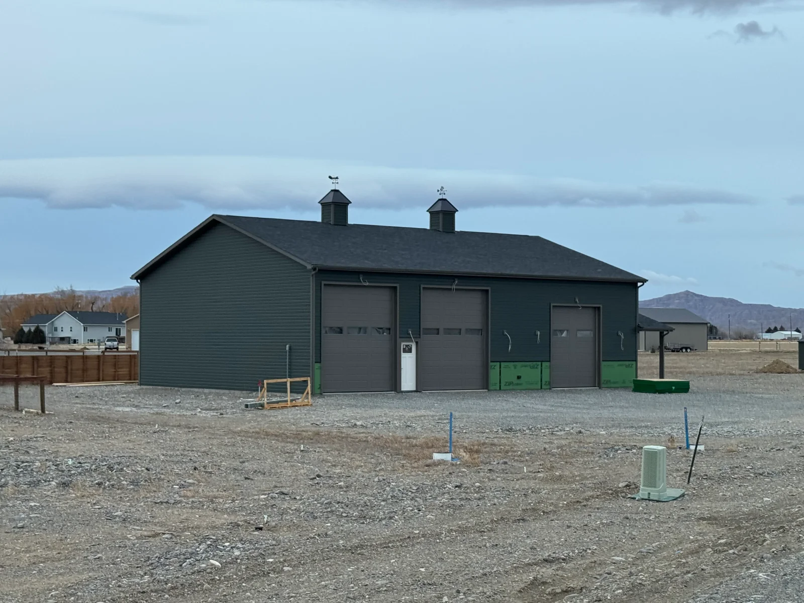 Dark gray vinyl siding agricultural building with multiple garage doors and cupolas