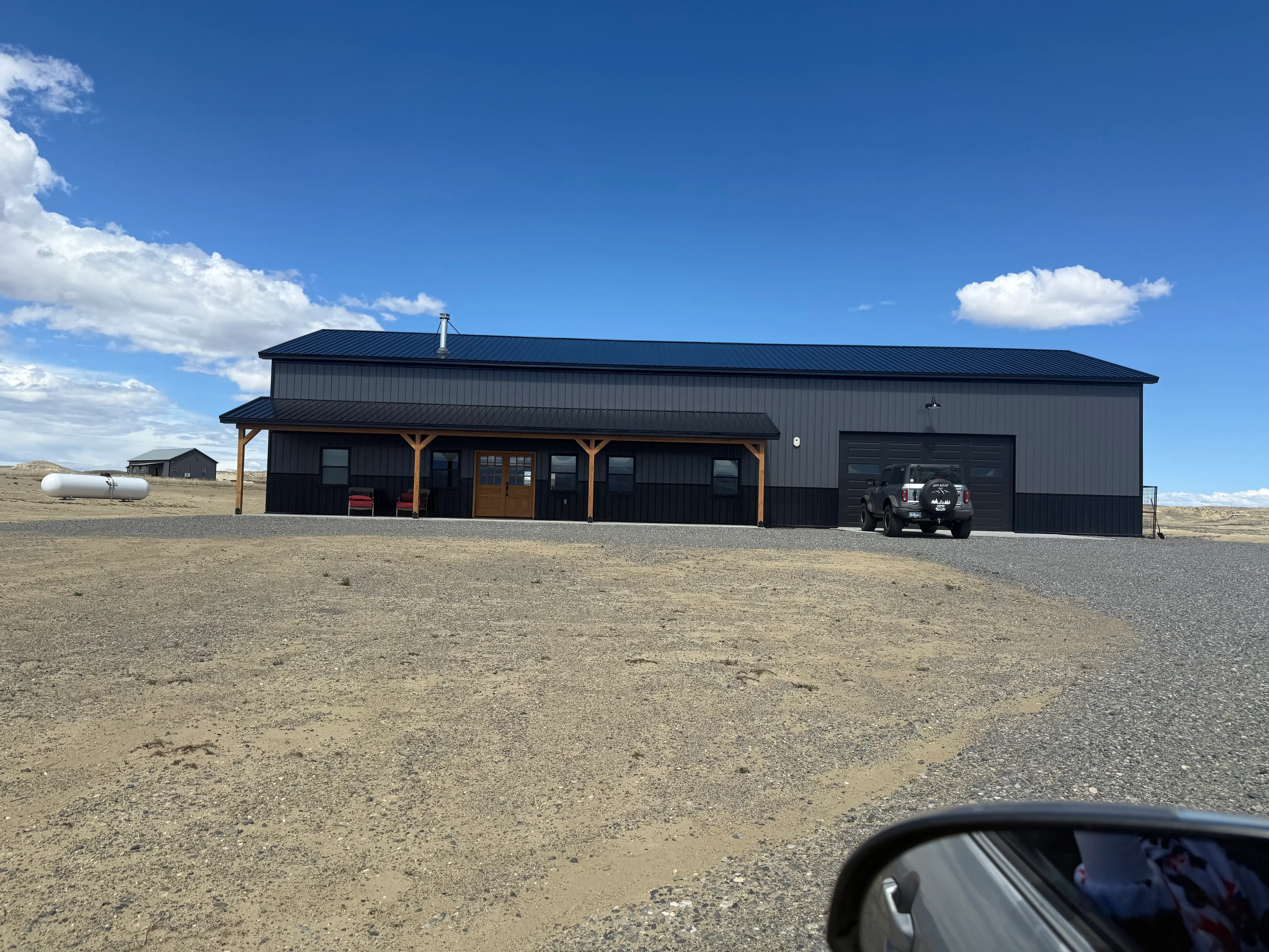 Metal-frame agricultural building with standing seam roof, corrugated siding, timber portico, and equipment garage