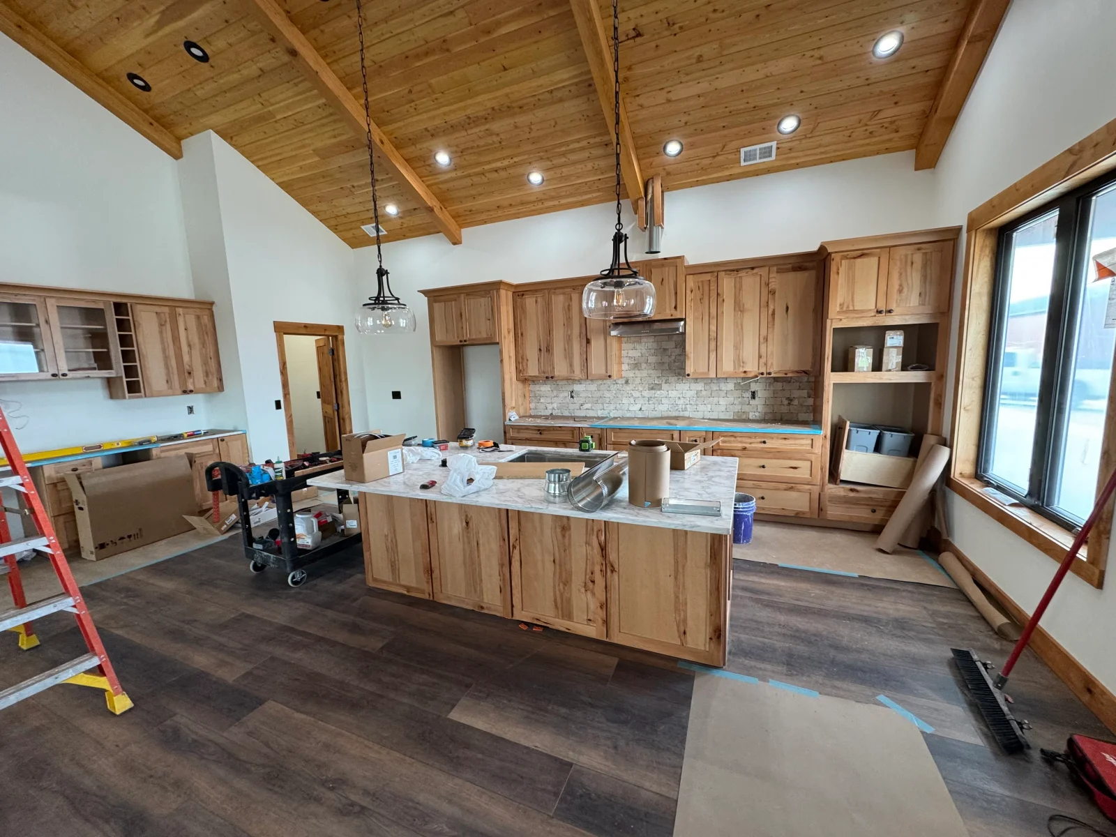 Kitchen with knotty alder cabinets, timber beams, marble countertops, and subway tile backsplash under construction