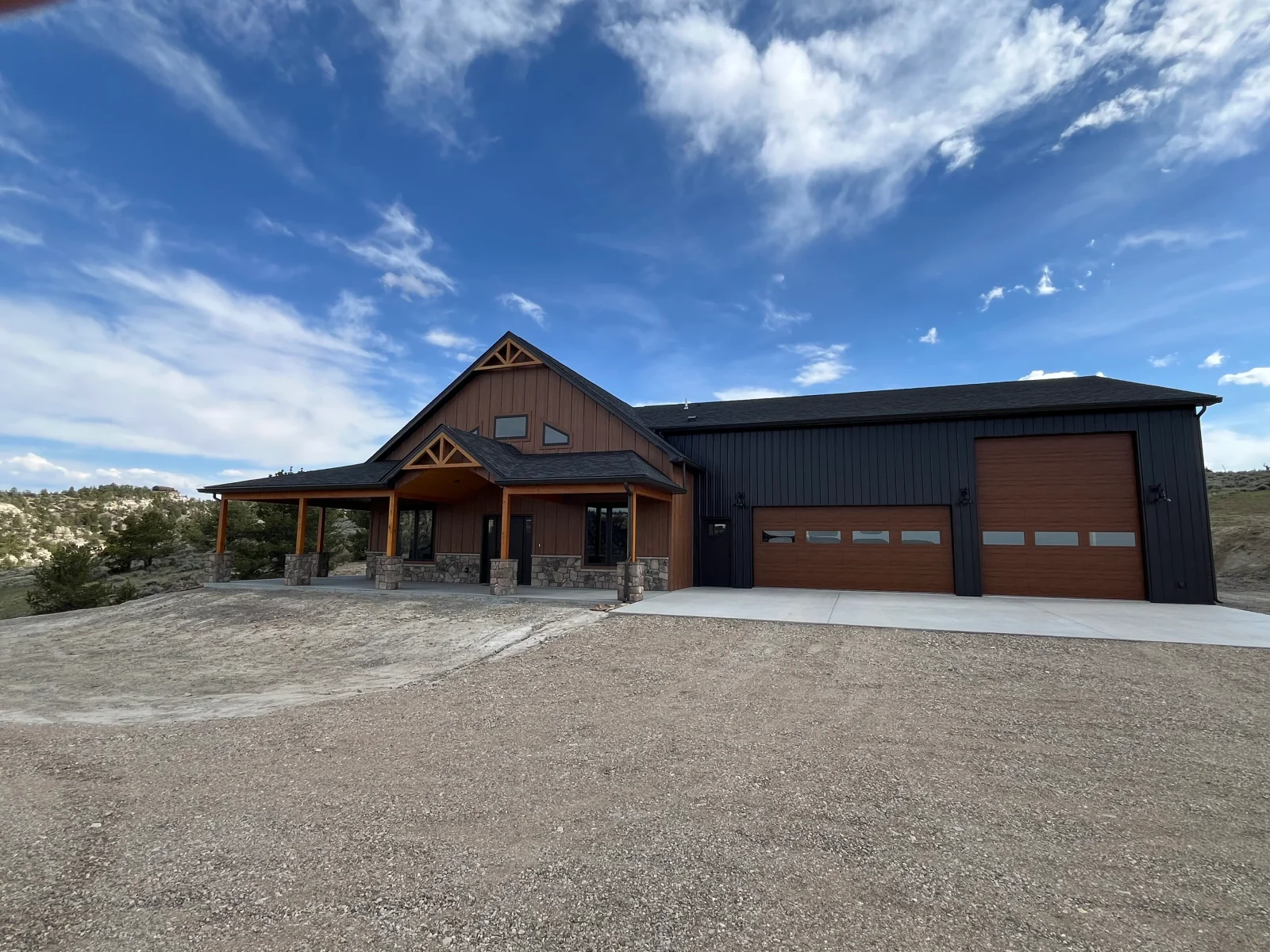 Modern home with timber posts, stone veneer, metal siding, and three-car garage on gravel driveway