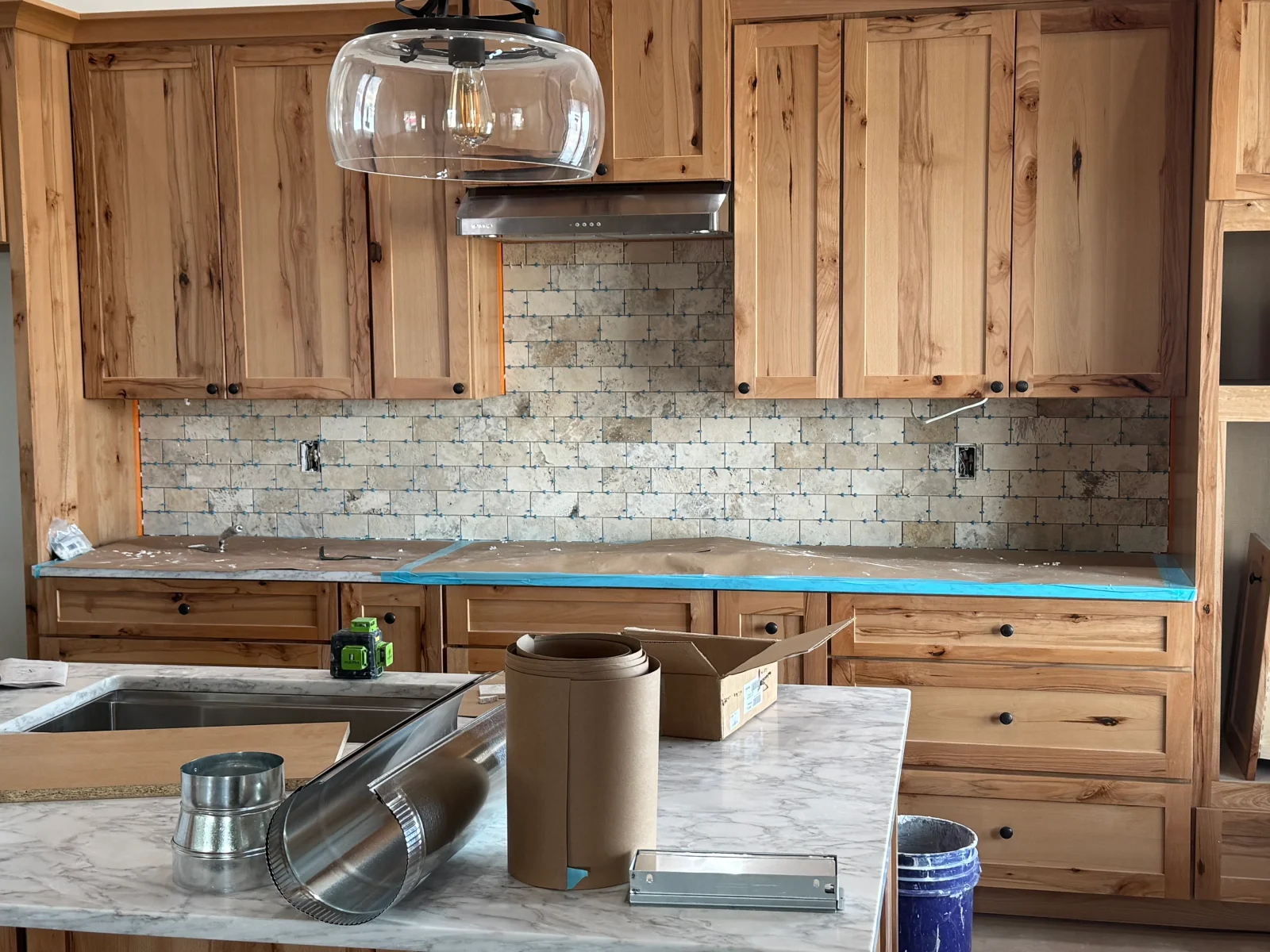 Kitchen with knotty alder cabinets, marble counters, subway tile backsplash, and stainless steel hood