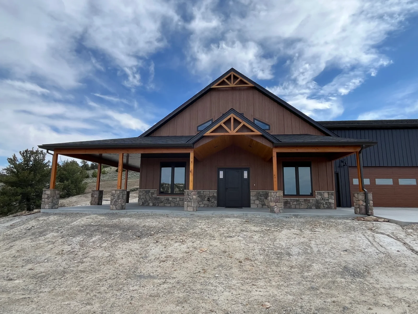 New residential home with stone veneer, metal siding, timber posts, and covered porch entry