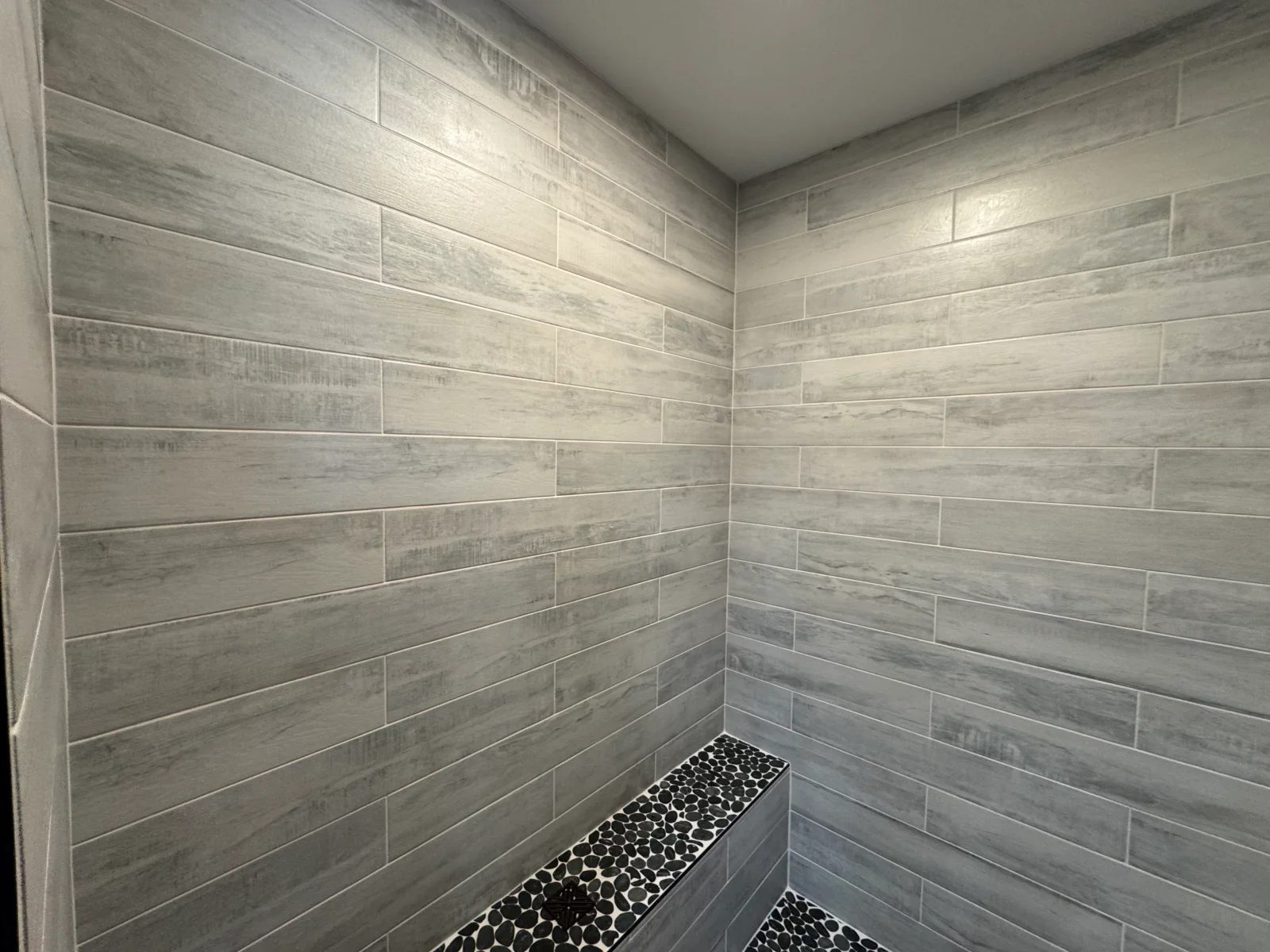 Gray wood-look porcelain tile shower walls with black pebble mosaic floor