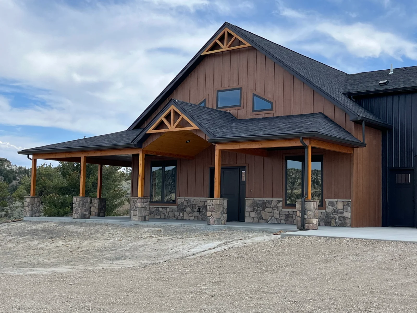 Modern home with brown metal siding, wood beams, stacked stone foundation, and covered porch